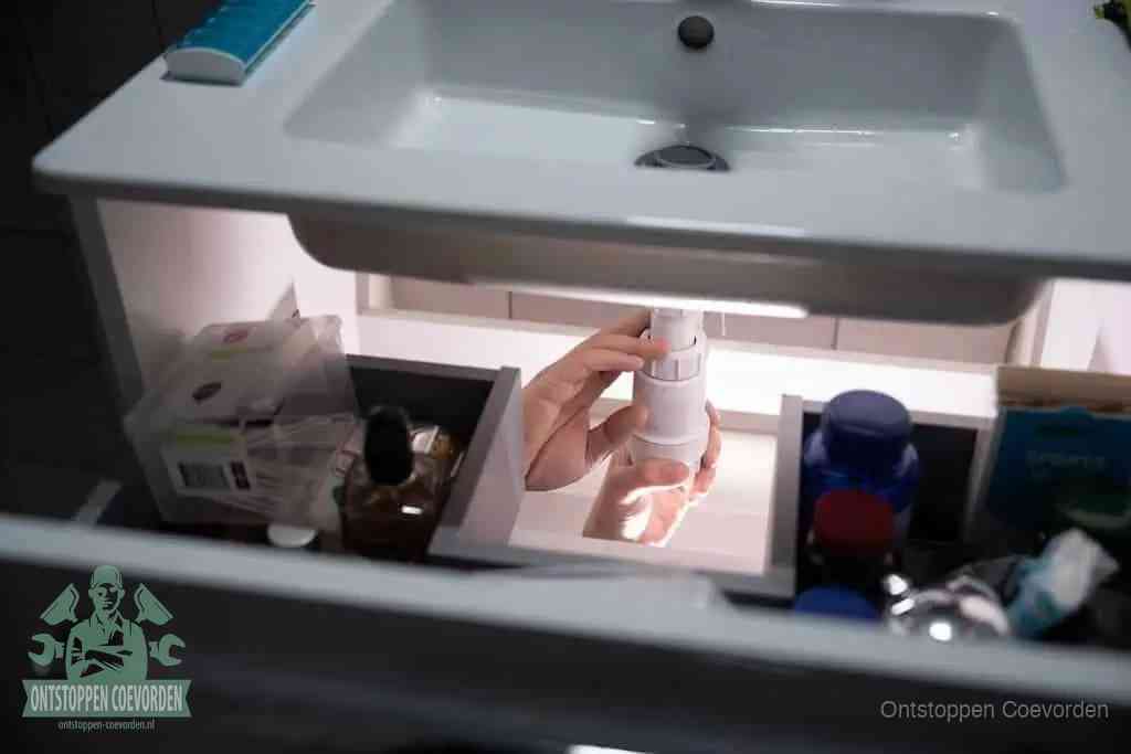 Een pompfles met zeep boven een wastafel, de heet water en afwasmiddel-methode om een vetprop in de afvoer los te maken in Coevorden