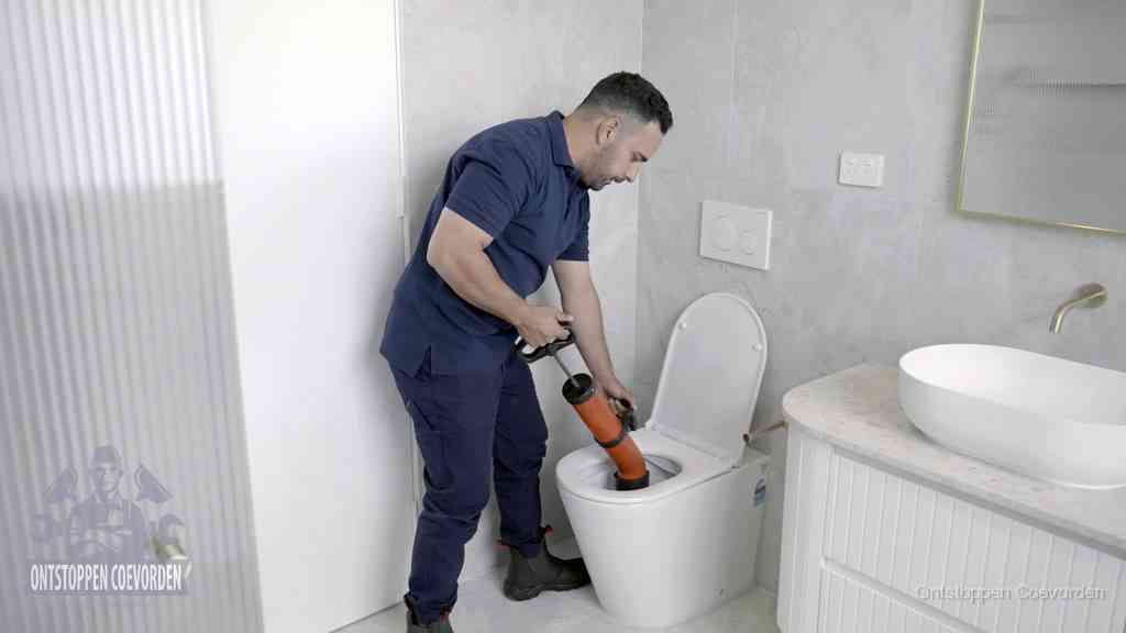 Een monteur buigt over een wandcloset en duwt met de hand een persluchtontstopper in de toiletpot om de verstopping handmatig los te maken in Coevorden