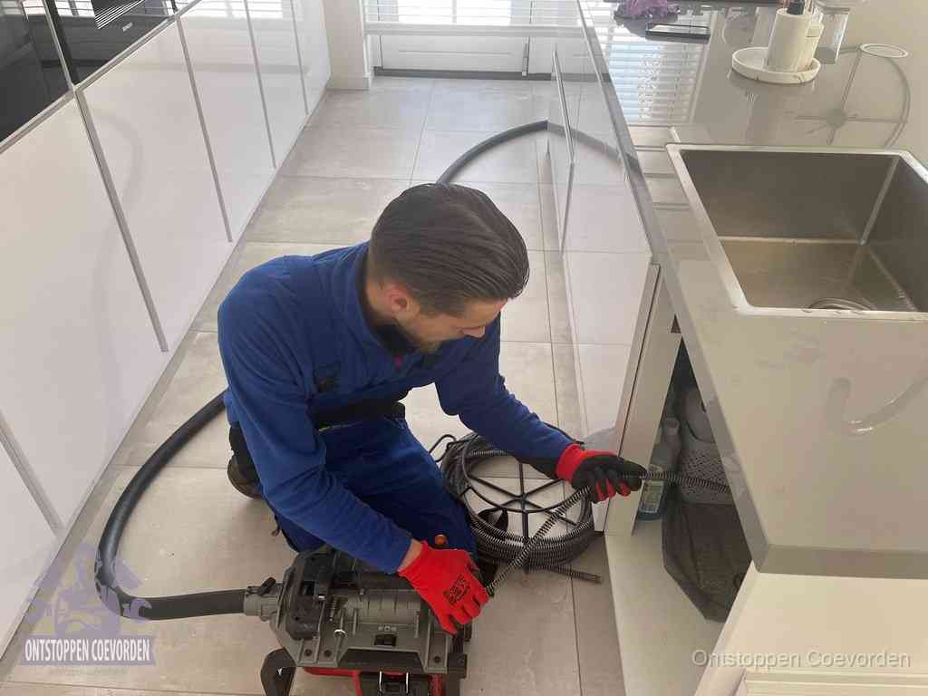 Een monteur ontstopt de keukenafvoer onder de spoelbak met een elektrische veermachine in Coevorden