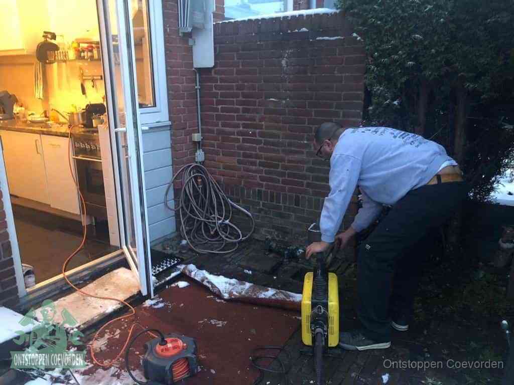 Een monteur werkt buiten bij een open riool-/grondput met een elektrische ontstoppingsmachine om een verborgen afvoerprobleem op te sporen in Coevorden
