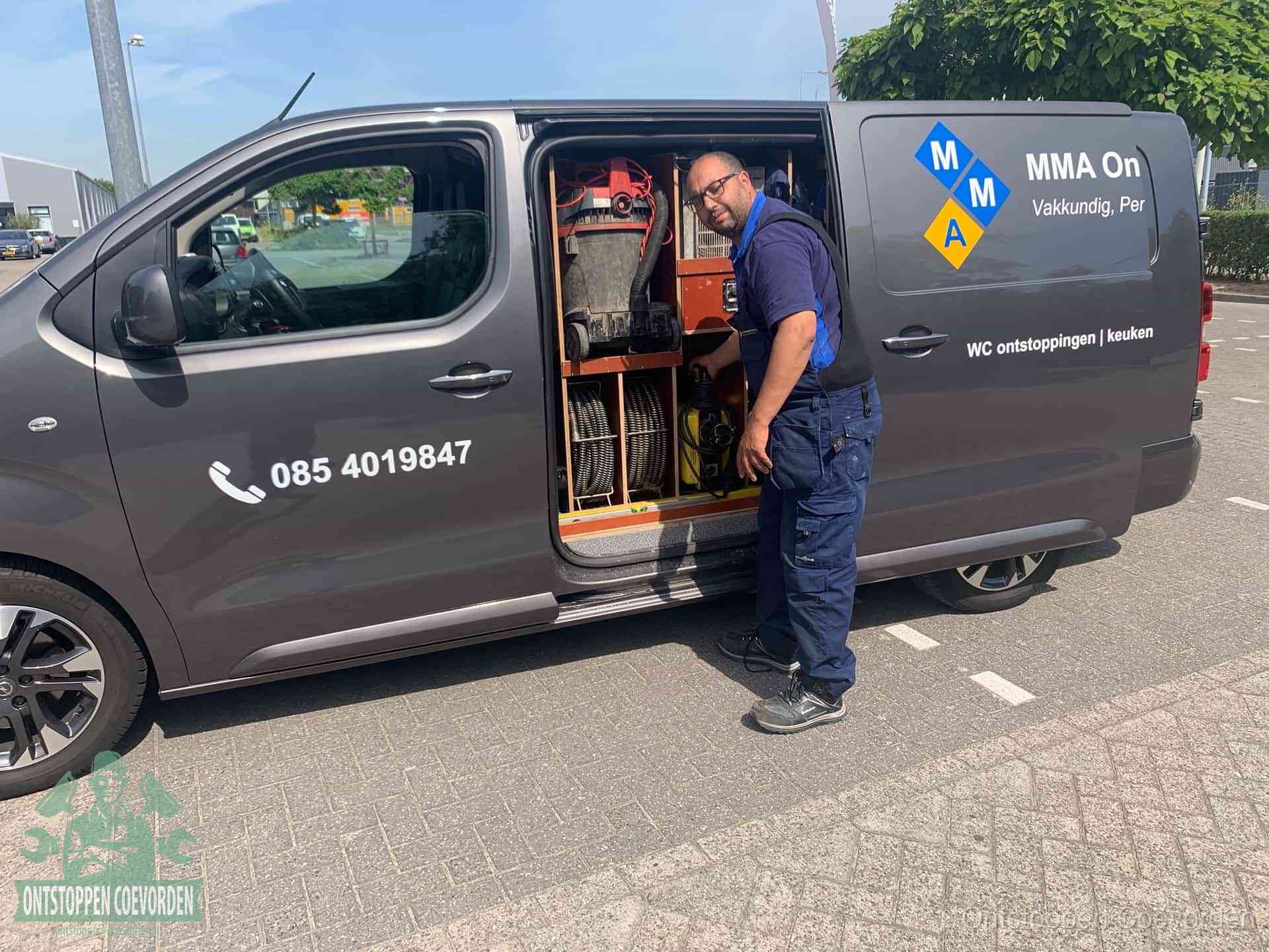 Een monteur bij de open schuifdeur van zijn bedrijfsbus op een parkeerplaats, klaar om de oorzaak van terugkerende afvoerverstoppingen aan te pakken in Coevorden