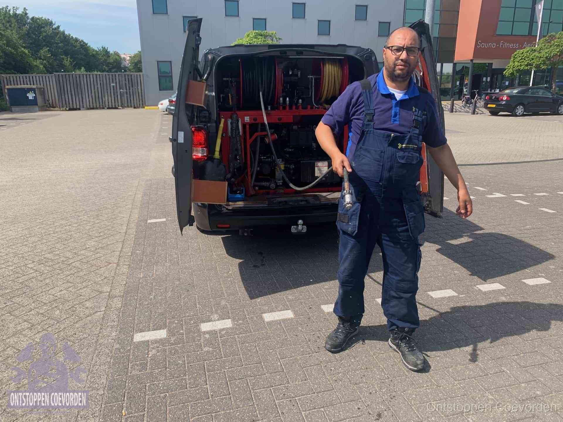 Een monteur bij zijn bestelbus met een hogedruk- en rioolreinigingsunit, klaar om de oorzaak van terugkerende wc-verstoppingen aan te pakken in Coevorden