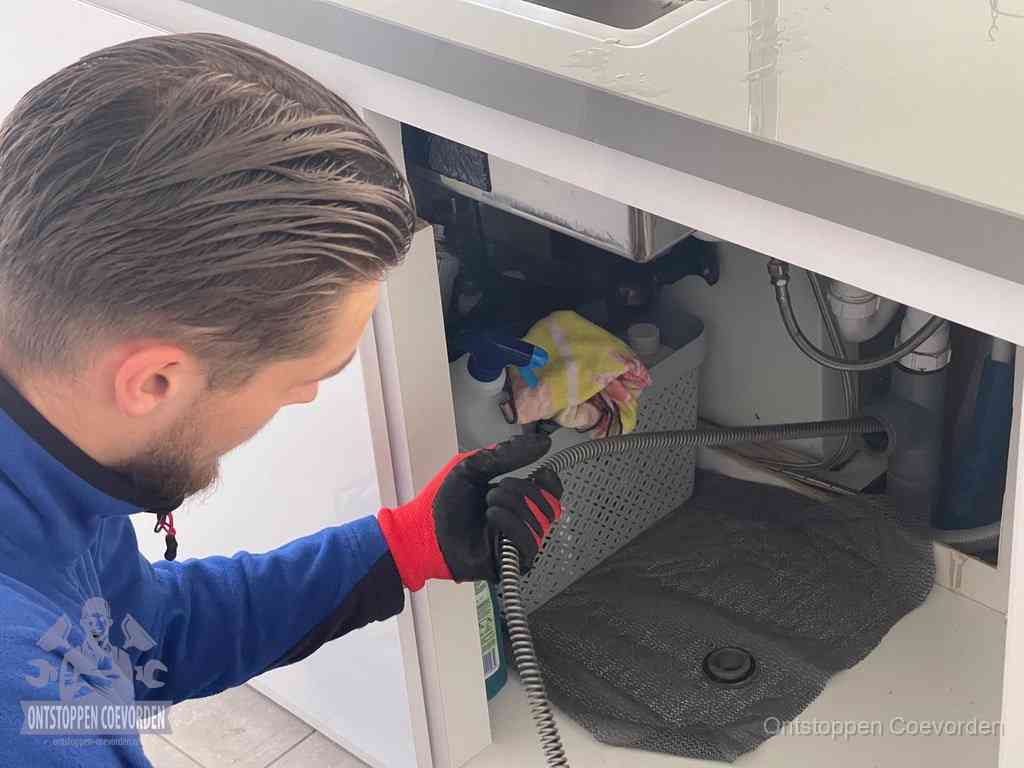Een monteur voert een flexibele ontstoppingsveer in de afvoer om een verstopping voorbij de bocht van het toilet te bereiken in Coevorden