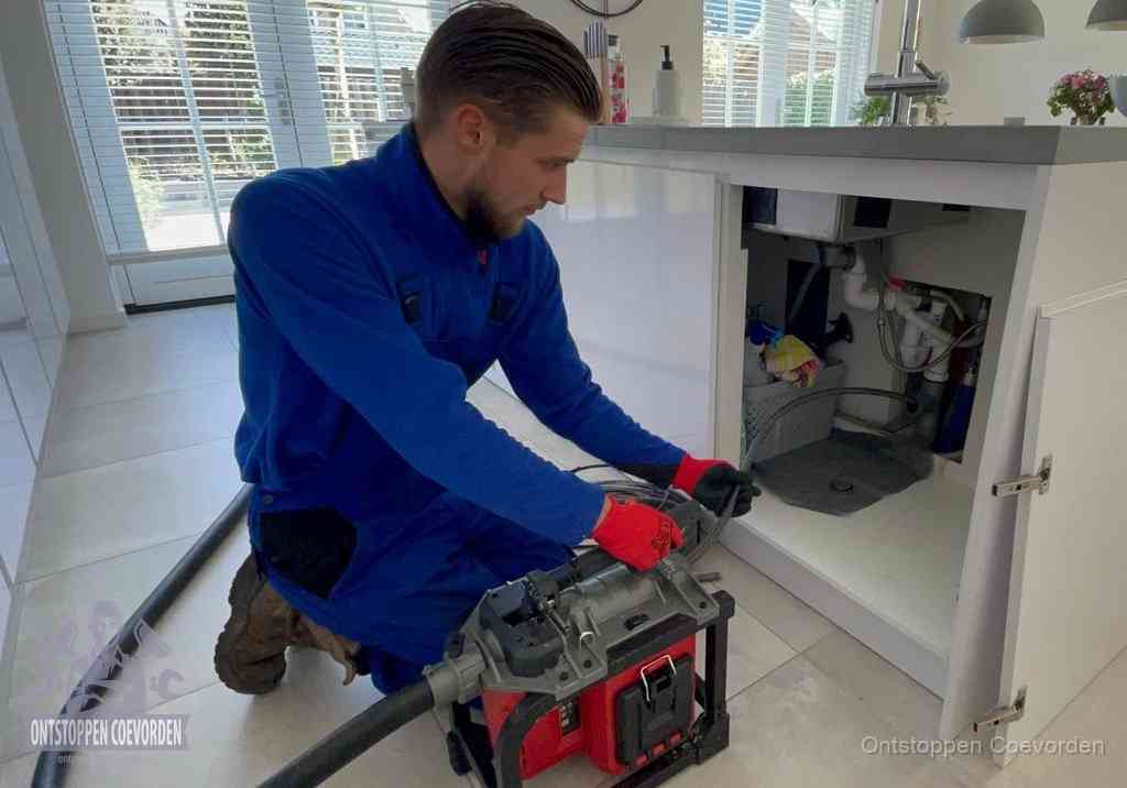 Een monteur voert een professionele elektrische ontstoppingsmachine in de afvoer onder de spoelbak tijdens het gootsteen ontstoppen in Coevorden
