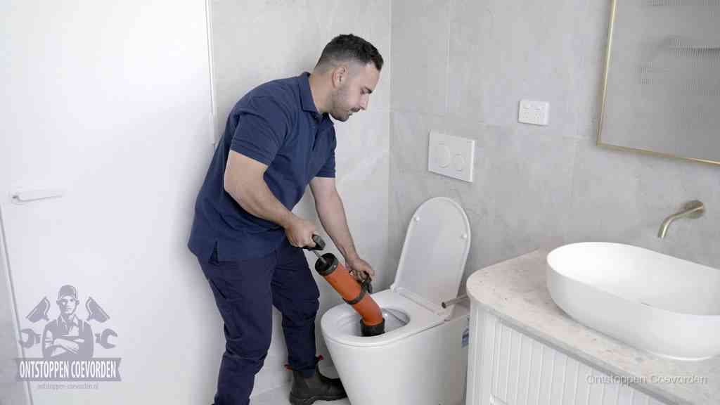 Een monteur gebruikt een handmatige perspomp (toiletontstopper) op een wandcloset tijdens het professioneel wc ontstoppen in Coevorden