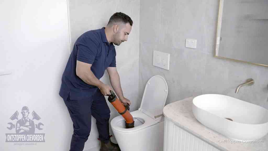 Een man gebruikt een handmatige luchtdruk-ontstopper in een modern betegeld toilet om zelf de wc te ontstoppen in Coevorden